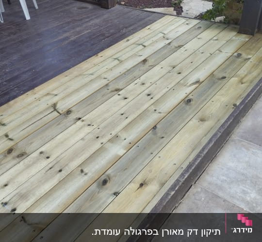 דק עץ חדש מותקן בגינה ליד שביל אבן